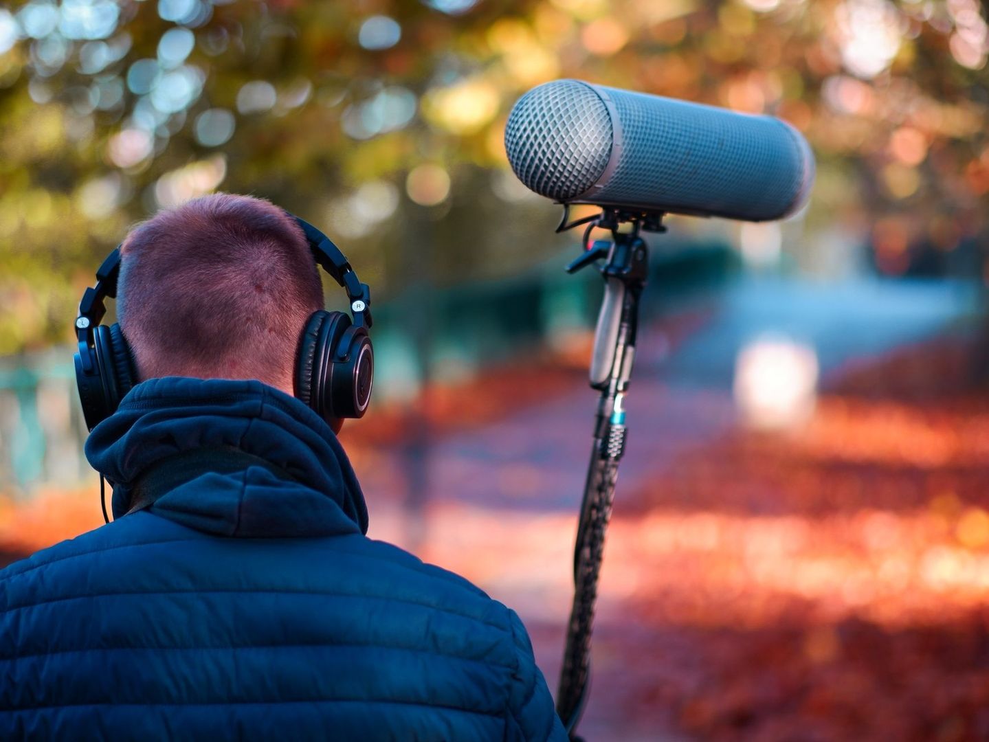 Person wearing headphones beside a large microphone outdoors